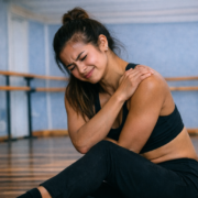 Dancer in pain in dance training holding shoulder in studio