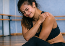 Dancer in pain in dance training holding shoulder in studio